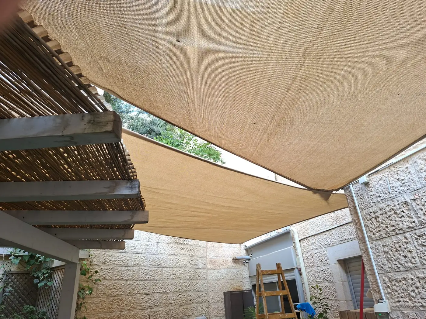 רשת הצללה מתחת לפרגולת עץ מול הגינה